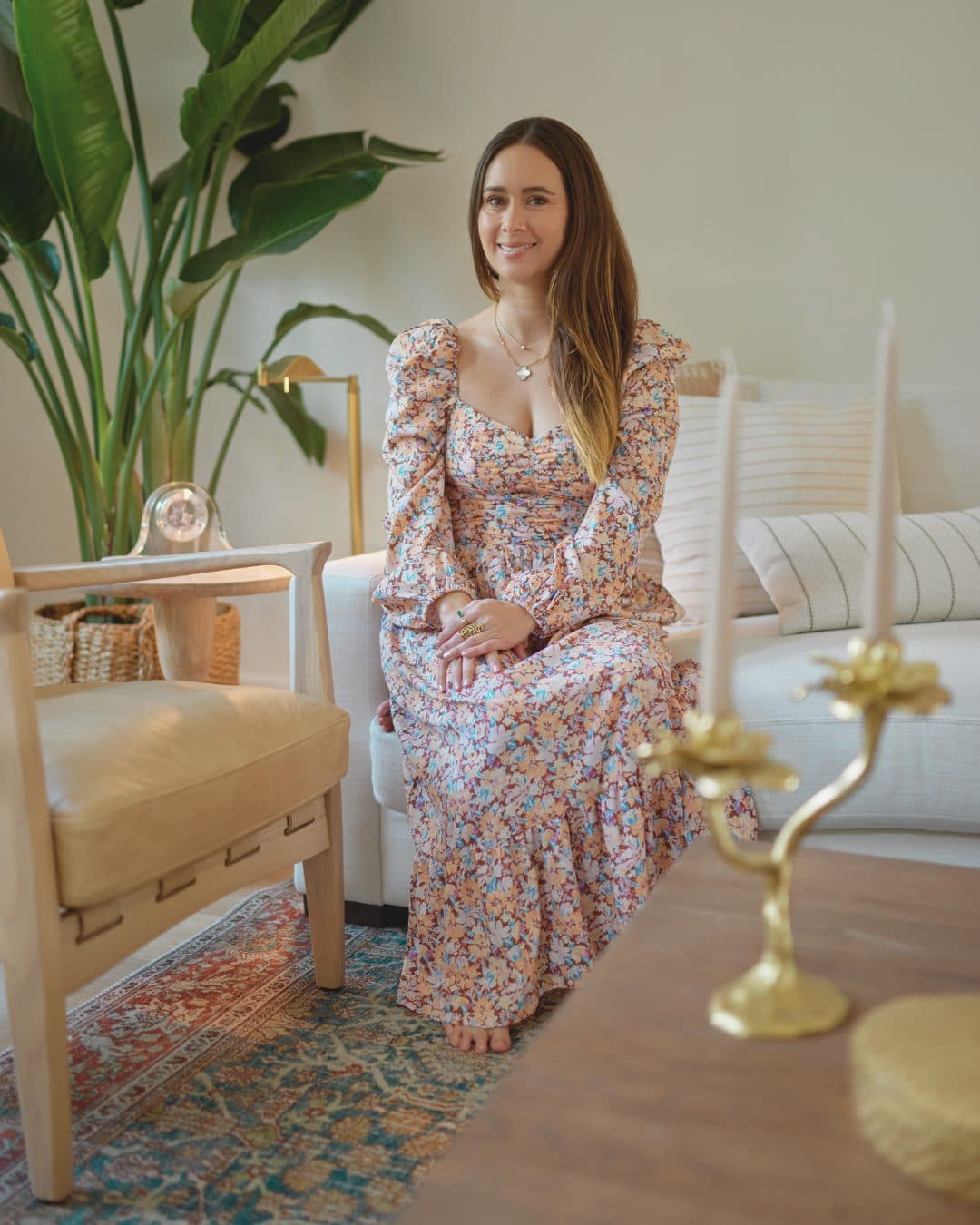 Paula sitting on a sofa between gold candlesticks and a tall plant
